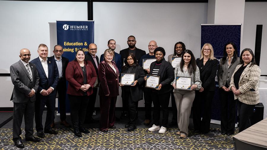 A large group of smiling people stand together. Some are holding certificates.