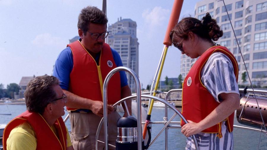 Three people are on a boat and are wearing lifevests.