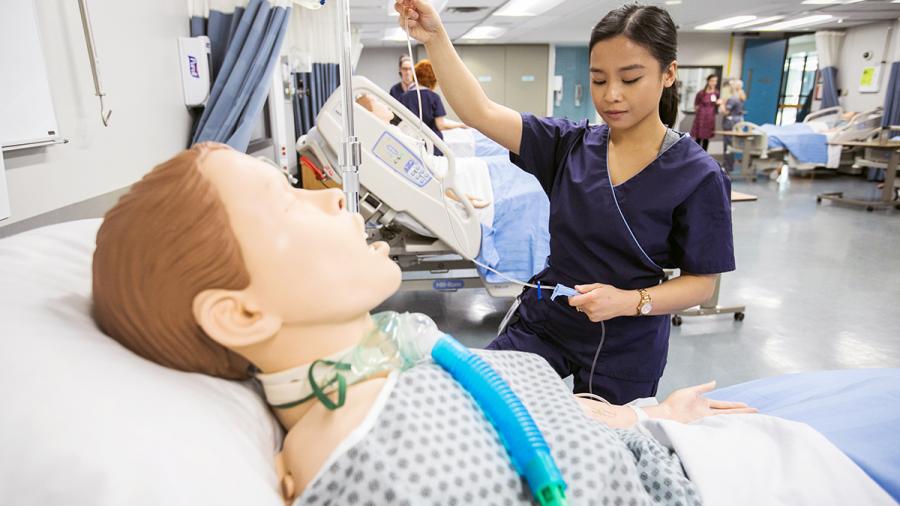 A student holds up an IV line that’s attached to a training dummy.