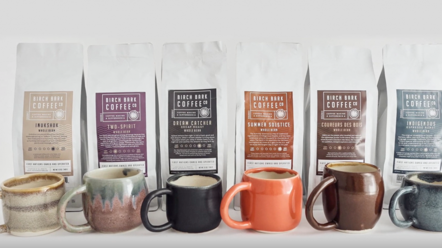 Six bags of Birch Bark Coffee Company coffee beans are lined up in a row with mugs in front of them.