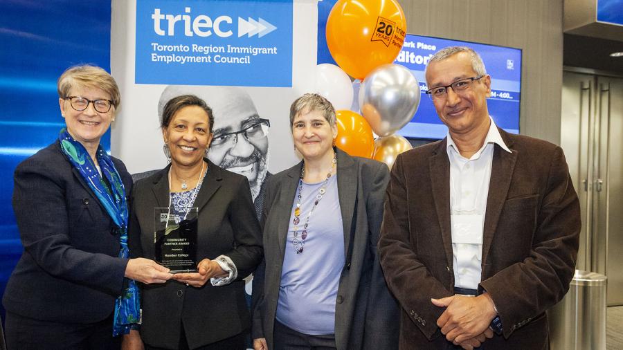 Four people stand together in front of a banner that reads TRIEC. Two are holding a trophy.
