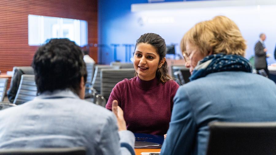 Three people sitting at a desk are having a conversation.