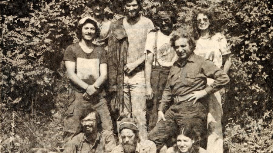 A group of people stand outside a forest and there are two dogs with them.