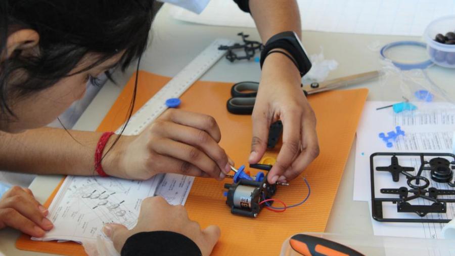 A student uses a tool on a mechanical device while another student looks at schematics.