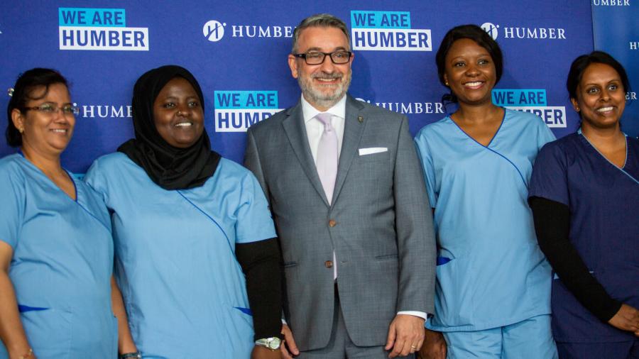 Five people pose for a photo in front of a backdrop that reads We Are Humber. Four of the people are wearing medical uniforms.