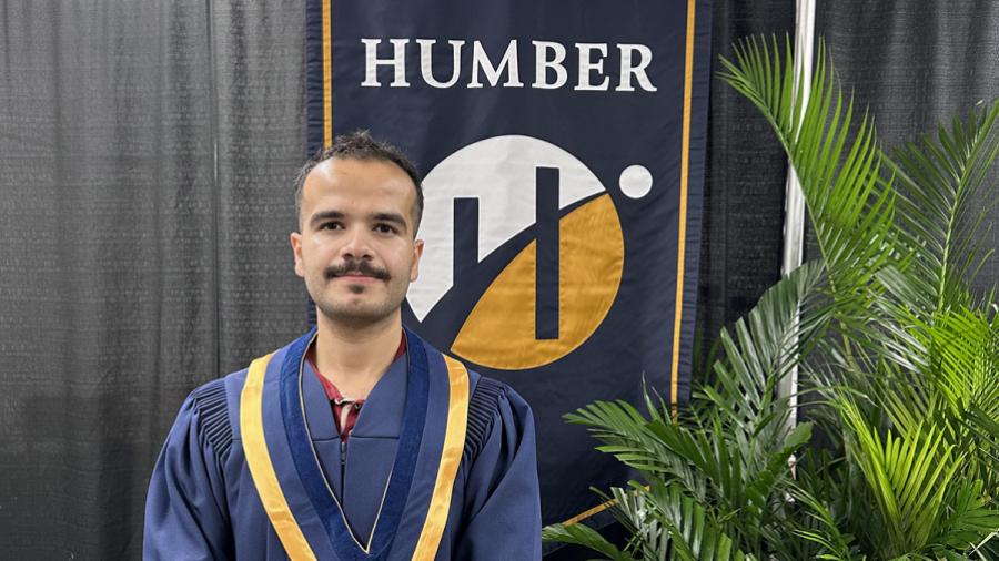 A person wearing convocation robes stands in front of a Humber Polytechnic banner.