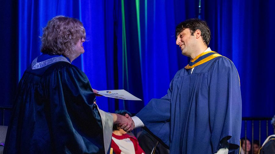 A person wearing a graduation robe receives a piece of paper from another person while on stage.