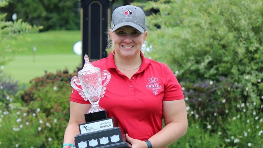 A smiling person wearing a red t-shirt with Canada written on it holds a trophy.