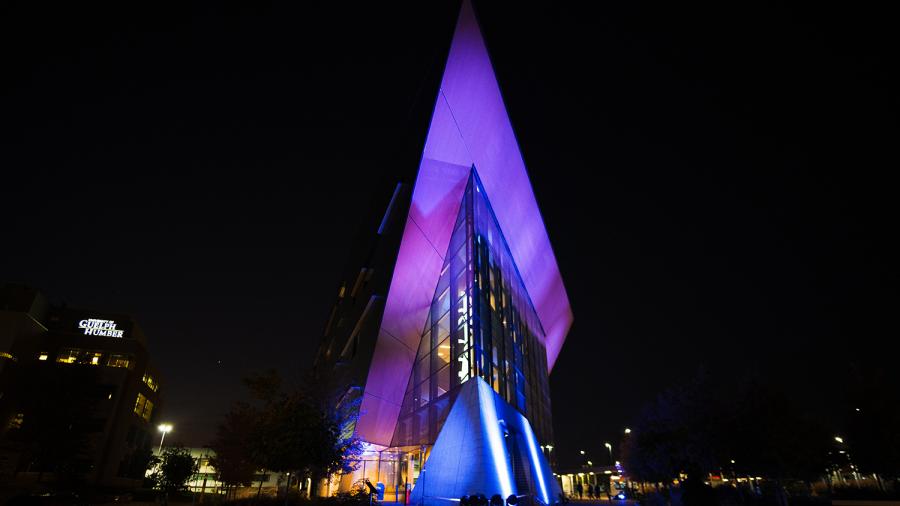 The exterior of a building at night that has the colours blue and purple being projected onto it.