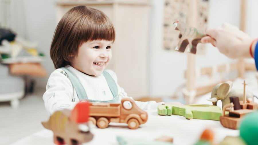 A child smiles and plays with a variety of toys on a table in front of her.