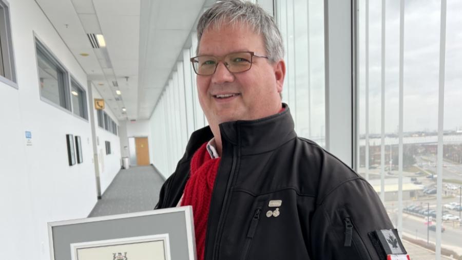 Mark Cameron stands in a hallway at Humber College and poses for a photo holding his 2022 Premier’s Award.
