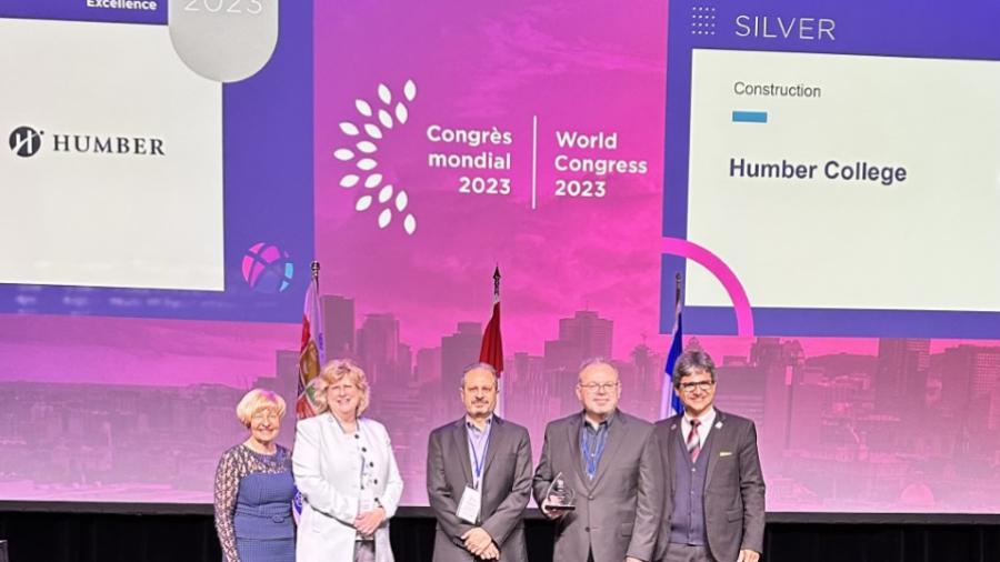 Five people, including Humber College president and CEO Ann Marie Vaughan, stand on a stage. One is holding an award.