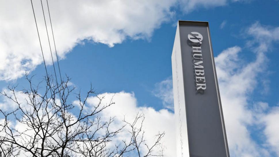 A tall pillar in front of Humber's Centre for Justice Leadership's is seen from below, against a cloudy sky, blue sky