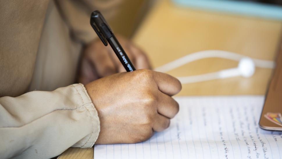A person holding a pen writes on a pad of paper.