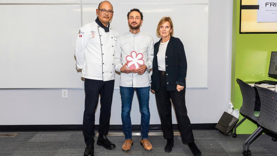 John-Vincent Troiano is the executive chef and owner of Michelin star-rated restaurant Frilu and he recently spoke to Humber College students. Three people, two of whom are wearing chef’s uniforms, pose for a photo. The person in the middle is holding an award.
