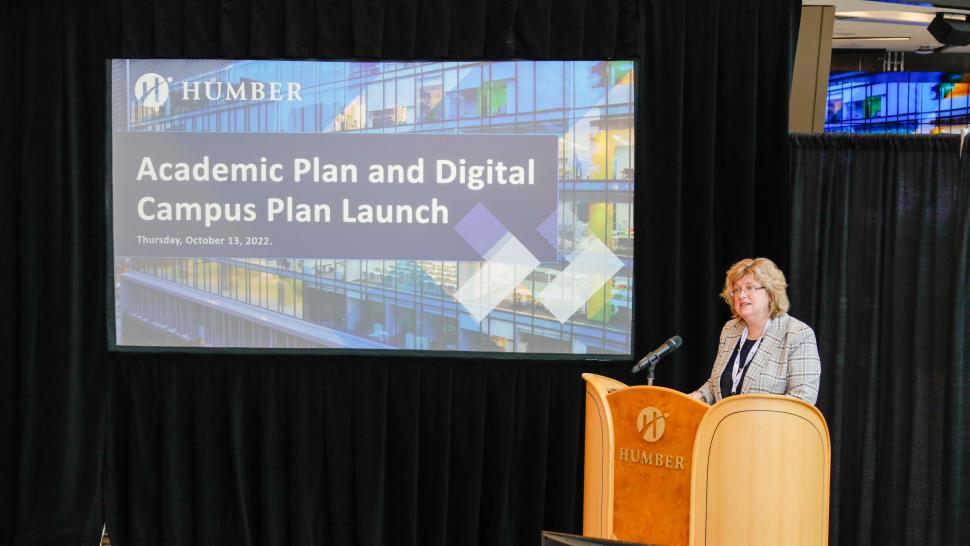 Dr. Ann Marie Vaughan stands at a podium in front of a screen that reads Academic Plan and Digital Campus Plan Launch.