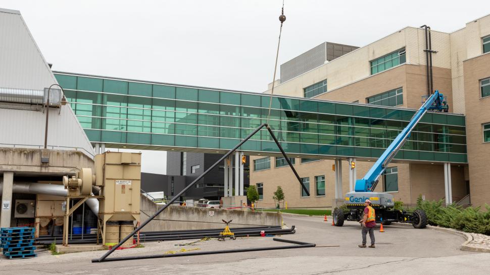 The construction crew working on the SWITCH project is making progress and, in August, lifted pipes to the top of the Guelph-Humber bridge, adding to the extensive network of pipes on campus. A person wearing a safety vest watches as a crane lifts a piece of pipe off the ground.
