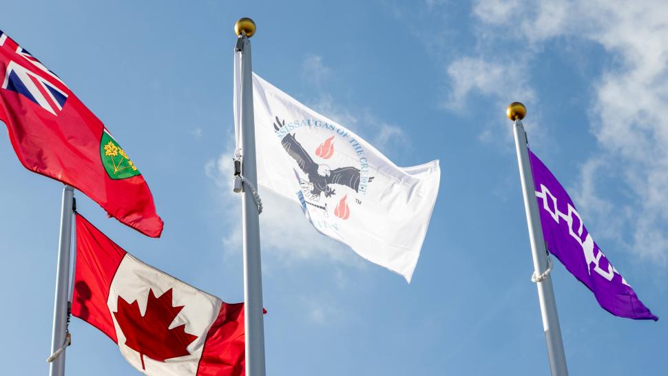 The Haudenosaunee Confederacy flag and the Mississaugas of the Credit First Nation flag are being flown at North Campus. Four flags fly against the backdrop of the blue sky.