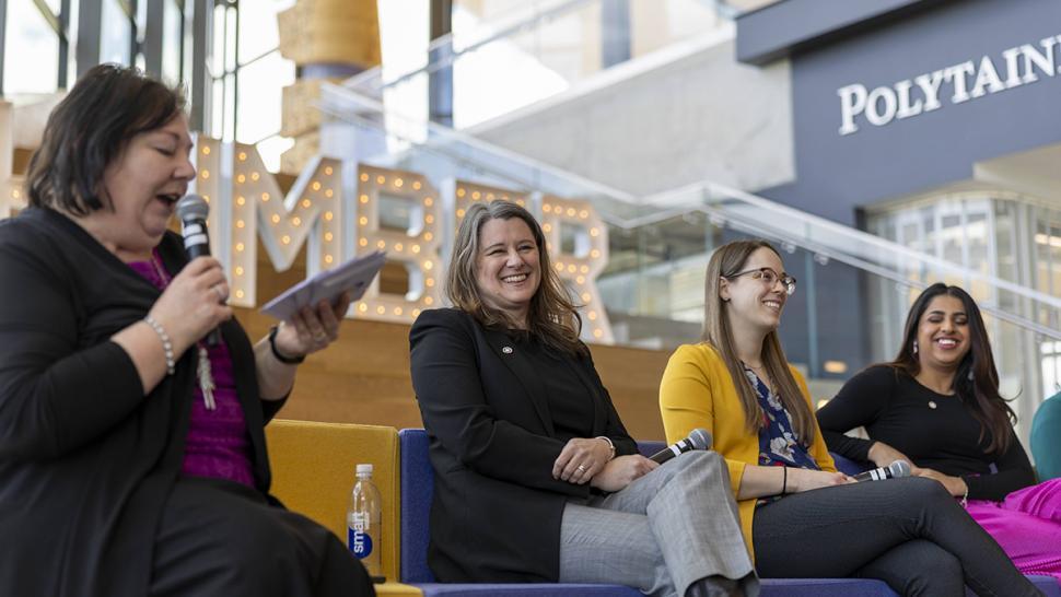 Several people on a stage are sharing a laugh while the moderator speaks into a microphone.