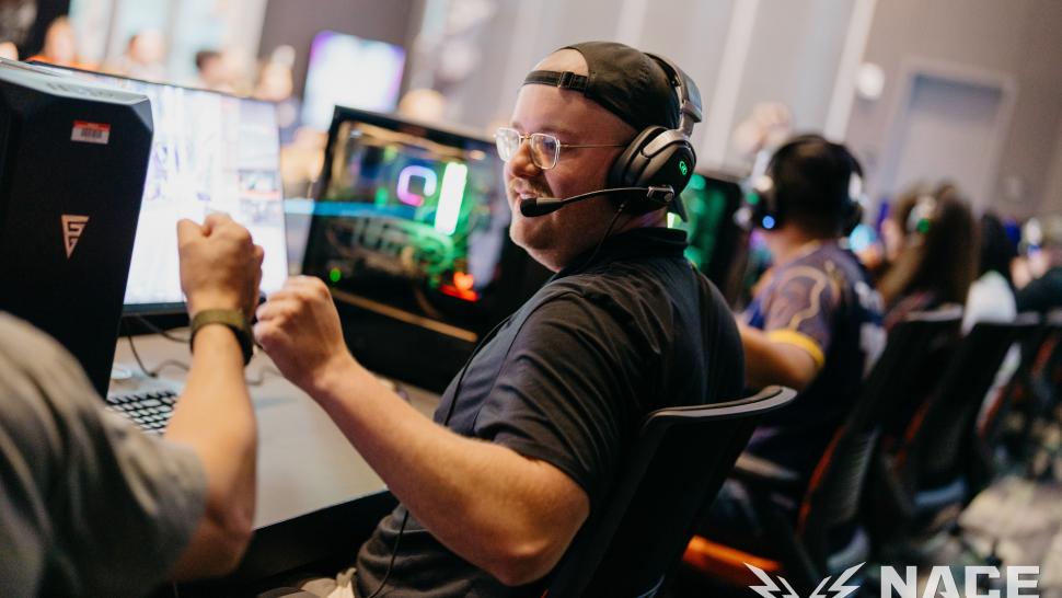 A row of people sit at gaming computers, two people fist bump in the forefront.