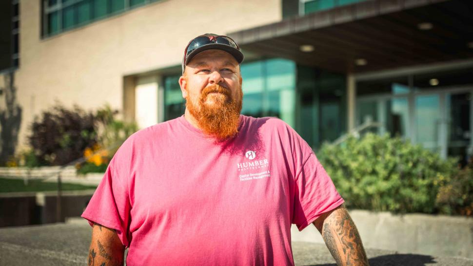 Scott Iles wears a pink shirt and poses outside the gardens in from of U of GH