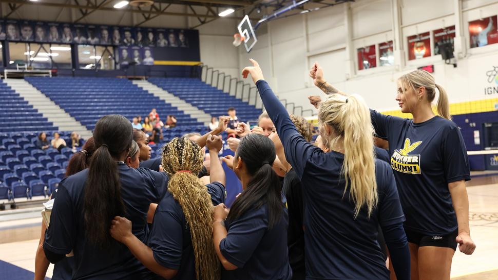 Athletes stand together in a huddle in a gym.