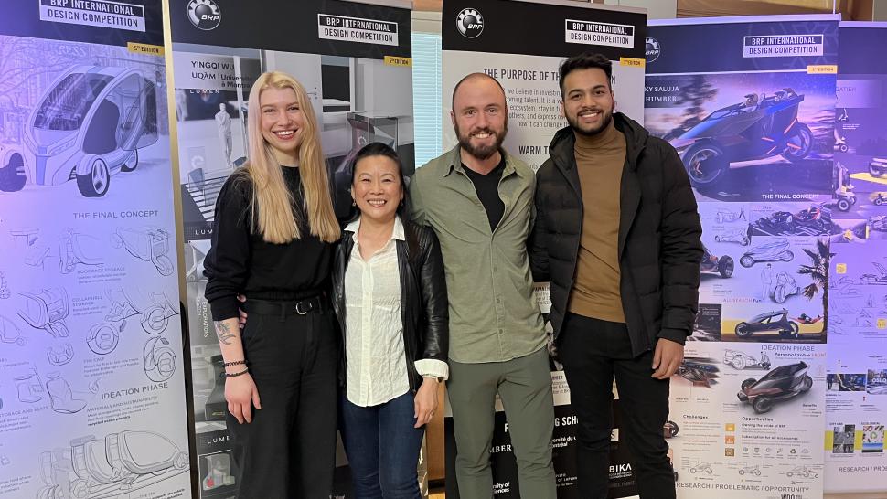 A group of four people stand in front of banners that read BRP International Design Competition.