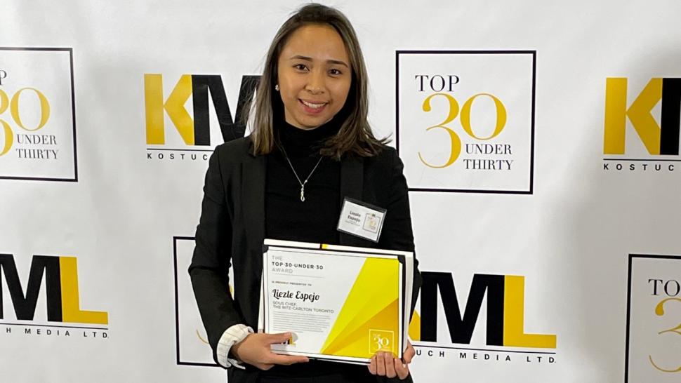 Humber College alumna Liezle Espejo has been named as one of Kostuch Media’s 2022 Top 30-Under-30 award winners. Liezle Espejo holds a certificate while standing in front of a sign that reads Top 30 Under Thirty.