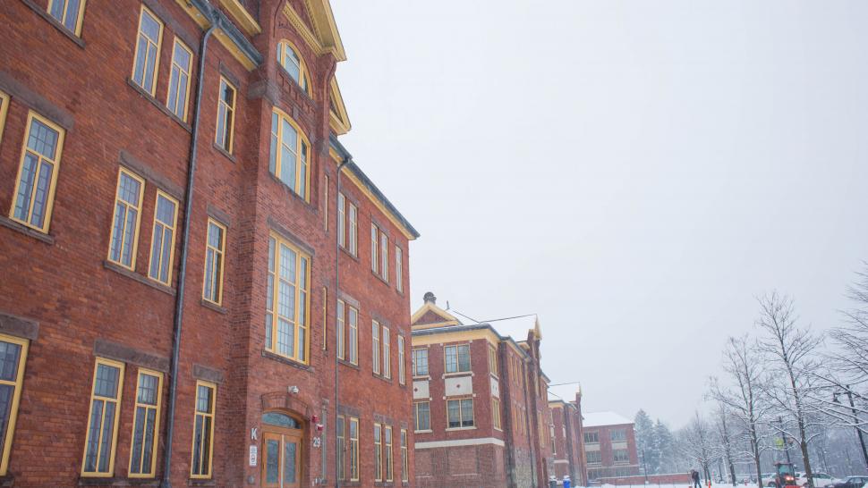 A brick building is shot from below against a grey sky with snow and bare trees