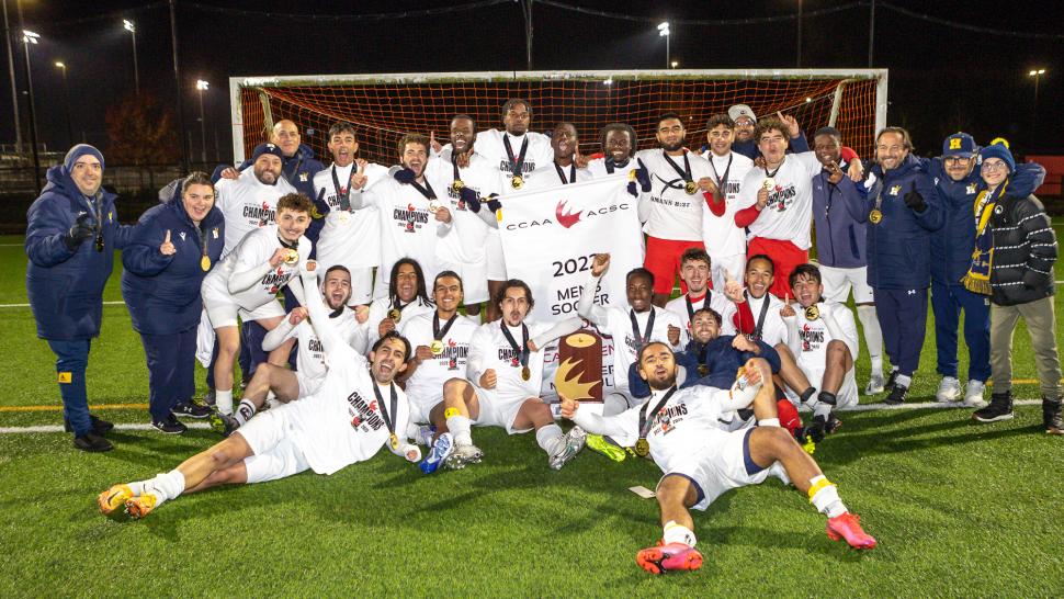 A group of Humber College soccer players and coaches celebrate while wearing gold medals.