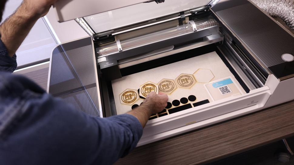 A person removes a piece of wood cutout from a printer that reads Idea Lab.