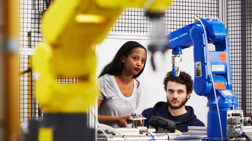 Two people look at a machine. One is holding a switch in their hand.