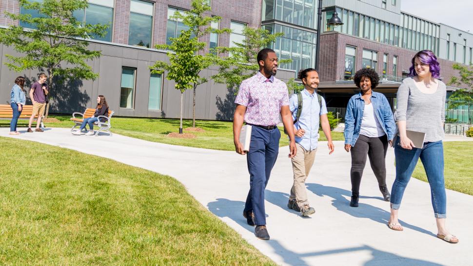 Students walk away from a building on Humber Lakeshore campus down a pathed path lined with grass on a sunny summer day