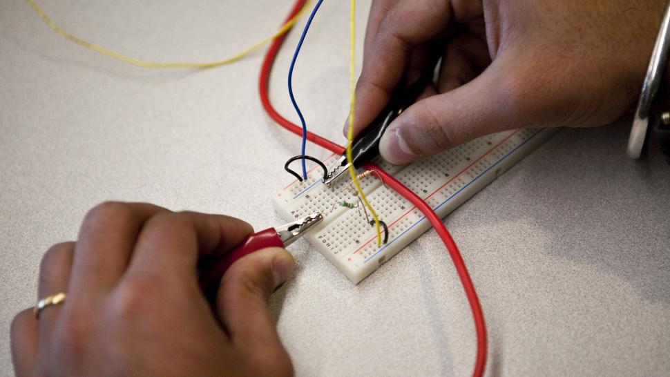 Two hands hold wires - one yellow, one red - together over a circuit board