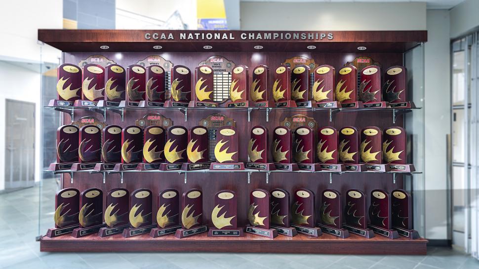 A large numbers of trophies in a trophy case that reads CCAA National Championships.
