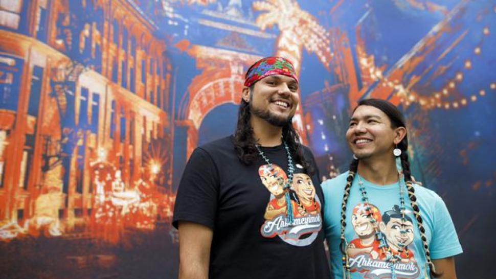 Anthony Johnson, left, and James Makosis, right, have their arms around each other, smiling and wearing long braids 