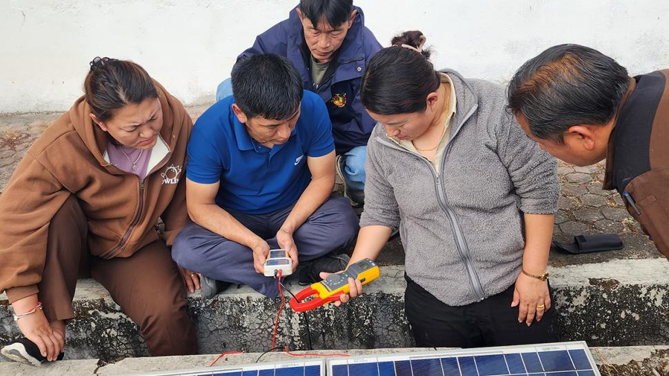 The Bhutan Education and Skills Training project is an initiative designed to transform Bhutan’s technical and vocational education and training system. Several people look at an electrical device that’s connected to a solar panel.