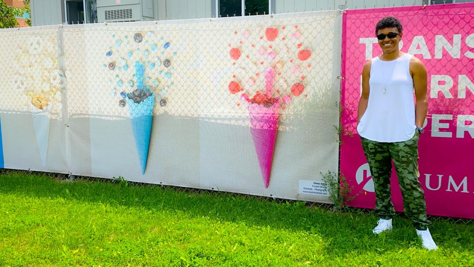 Krystal Moodie stands in front of her Cones piece - three coloured ice cream cones surrounded by candy and fruit