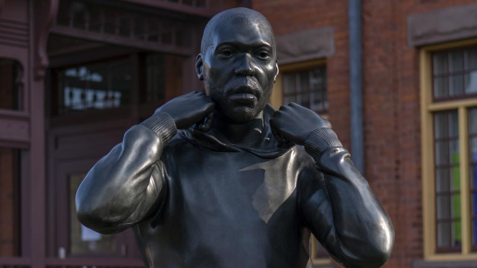 Cover Up (The Reveal), Thomas Price's 9-ft bronze statue of a Black male walking, pulling his hood up, stands outside C Cottage