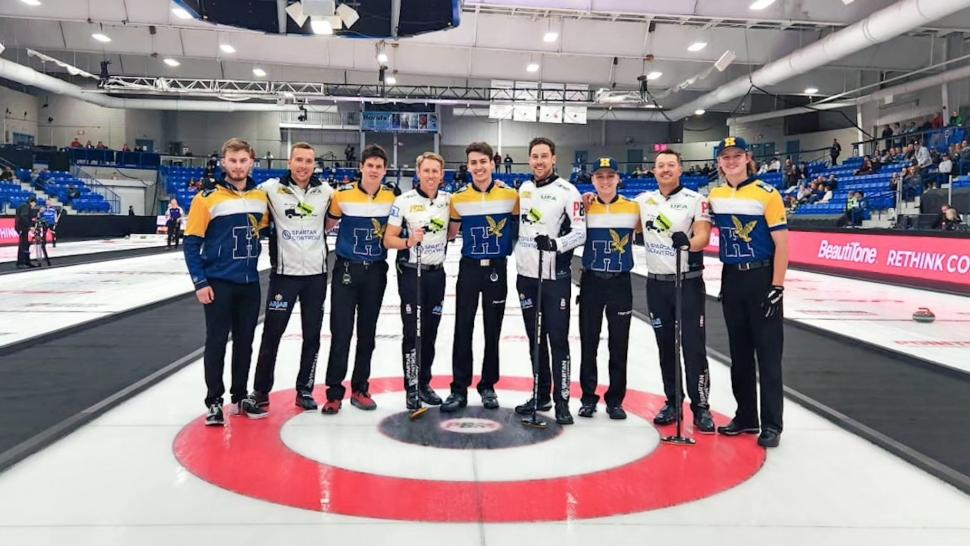 Two teams of people wearing curling jerseys and carrying brooms stand in a row.