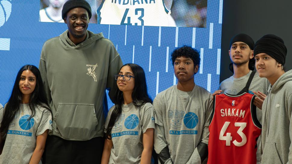 A person stands with a group of youth. One of them is holding up a jersey with the name Siakam and the number 43 on the back.