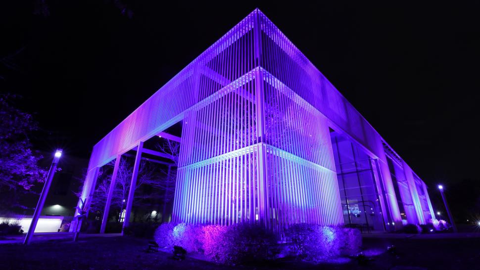 A photo of a building at night that has the colours blue and purple projected onto it.