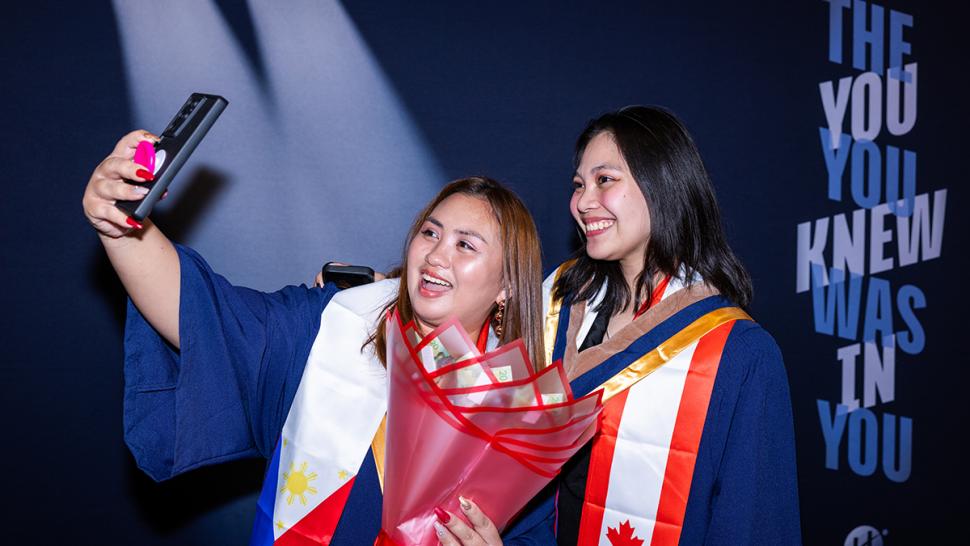 Two smiling people wearing graduation robes take a selfie.