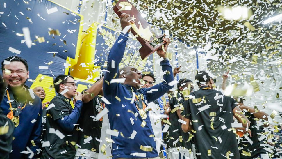 Humber Hawks' men's basketball team raise the national championship trophy while confetti flies around.