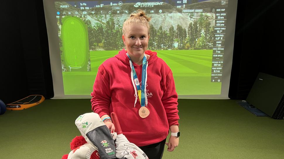 A golfer wears a bronze medal around their neck while standing in front of a golf bag filled with clubs. 