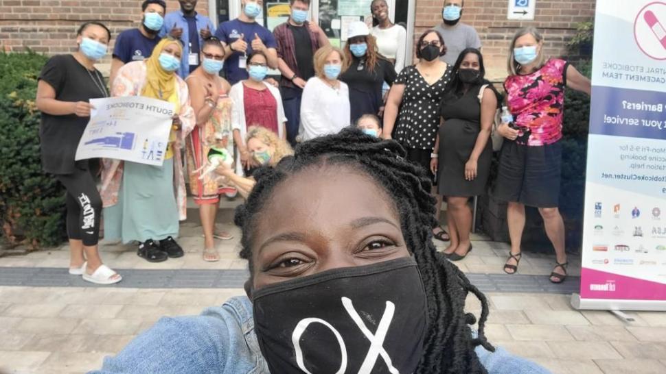 The vaccination clinic team at Lakeshore stands with masks on behind a woman taking a selfie, centered in the frame.