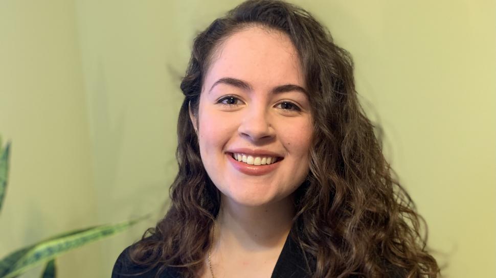 Nicole Pantaleo smiles in a headshot in a white shirt and black blazer. She has long curly hair parted on the side