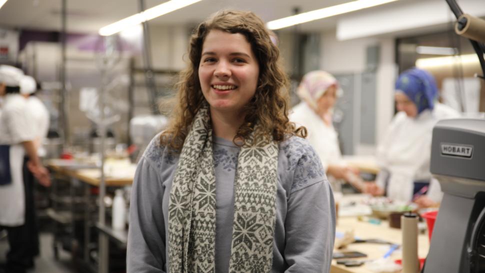 Stefanie Francavilla stands in the middle of a culinary lab at Humber with her arms crossed. She is smiling.