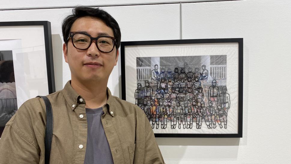 A person stands next to a piece of art on display on a white wall.