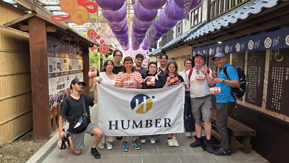 A group of smiling people are holding up a Humber Polytechnic flag.